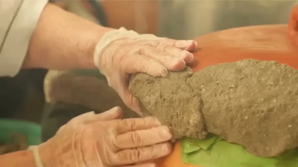 Mãos vedando uma panela de barro com massa de farinha durante o preparo tradicional do barreado.