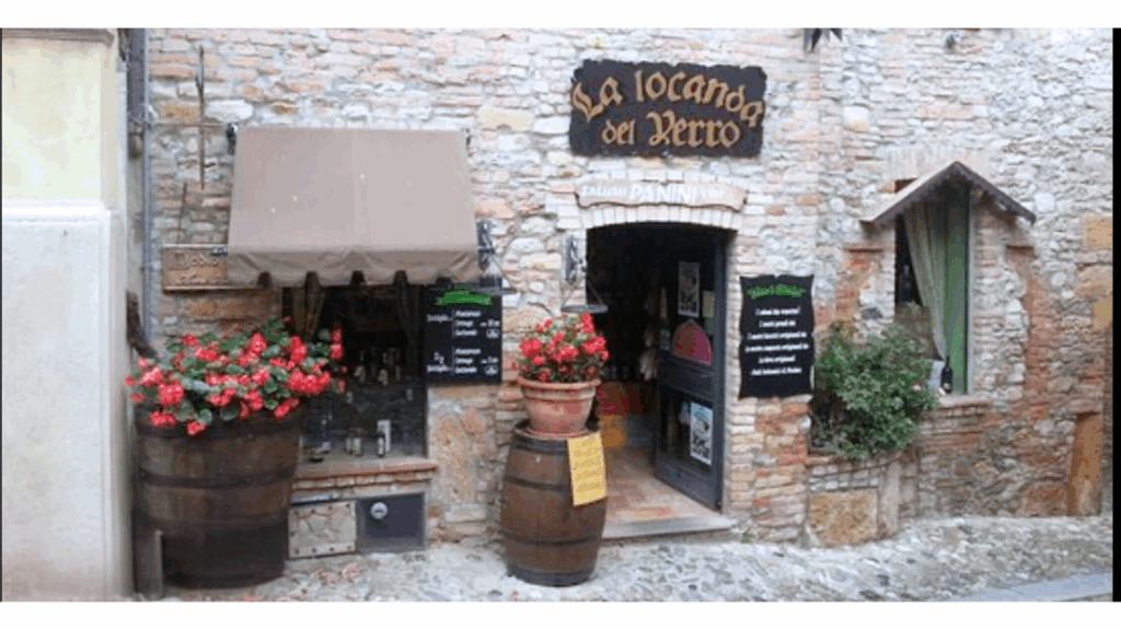 Fachada rústica de restaurante típico na Itália com flores, barris e letreiro “La Locanda del Verro” — gastronomia tradicional em ambiente acolhedor.