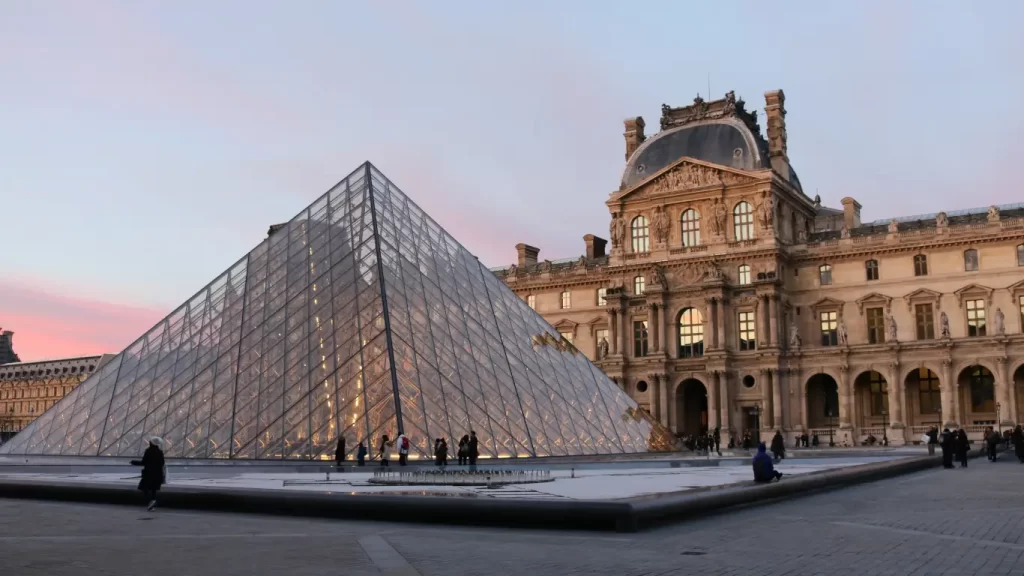 A icônica Pirâmide de Vidro do Museu do Louvre, em Paris, é um marco arquitetônico que combina modernidade com história. Projetada por I. M. Pei e inaugurada em 1989, esta estrutura de vidro e metal contrasta belamente com o clássico Palácio do Louvre, criando um ponto de encontro imperdível para viajantes. Dentro dela, os visitantes acessam as vastas galerias que abrigam tesouros como a Mona Lisa. O pôr do sol reflete maravilhosamente no vidro, tornando este momento especial para fotos e contemplação. Dica de viagem: Chegue ao entardecer para capturar a luz dourada e evite os horários de pico com reservas online.