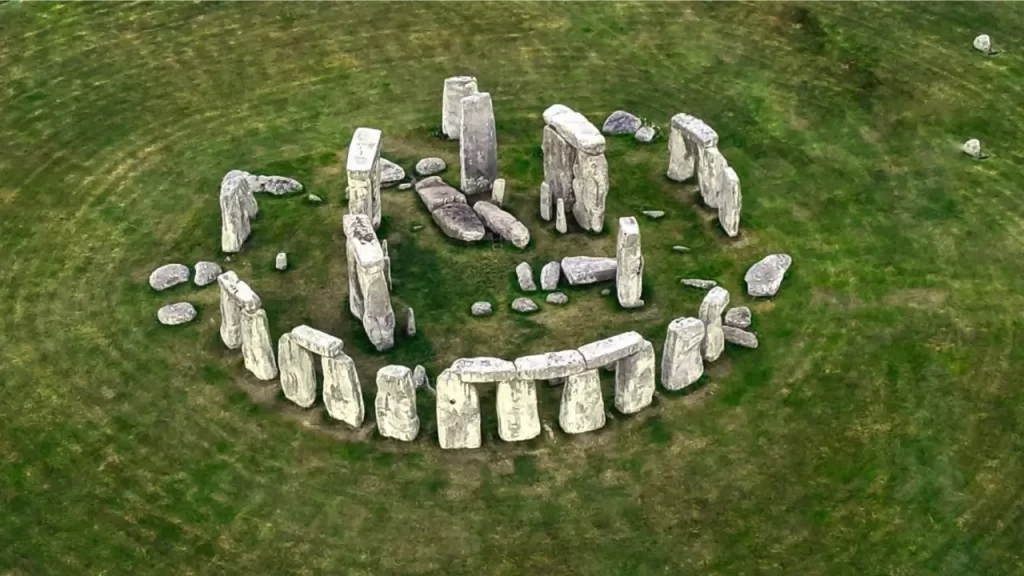 Uma vista aérea de Stonehenge, um círculo de grandes pedras pré-históricas dispostas em um gramado verde, com algumas pedras verticais e outras caídas.