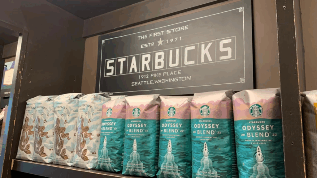Pacotes de café Starbucks em prateleira sob placa da primeira loja da marca, inaugurada em 1971 em Seattle.